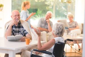 Elderly man and woman in a wheelchair sitting at a table with other people in the background