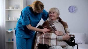 Caregiver covering an elderly woman with a blanket while she sits in her wheelchair